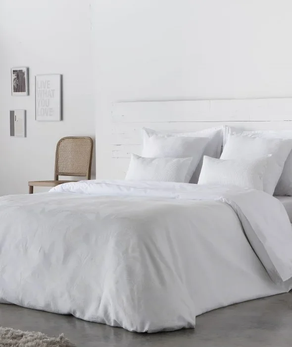 Housse de couette ANGELO en satin 300 fils 100% coton, mise en valeur sur un lit moderne.